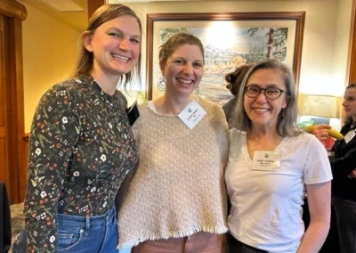 Oregon Geriatrics Society 2023 Conference - three attendees pose for a photo in front of a lovely painting of a mountain scene with trees and a lake