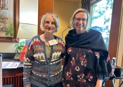 Oregon Geriatrics Society 2023 Conference - two attendees pose for a photo near a window showing a bright forest scene outdoors - rustic lodge