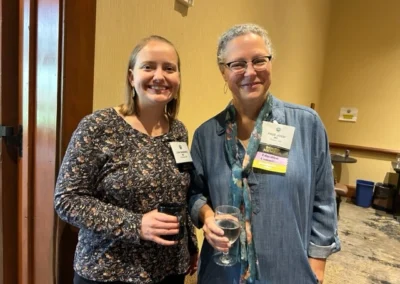 Oregon Geriatrics Society 2023 Conference - two attendees holding drinks and posing for a photo op in the entryway of a room in a rustic meeting lodge