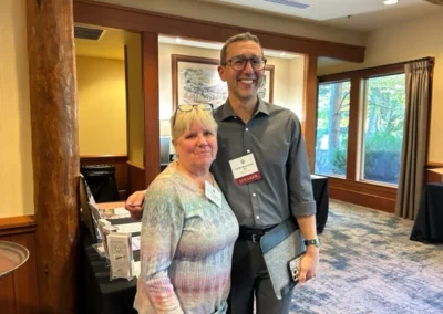 Oregon Geriatrics Society 2023 Conference - two attendees pose for a photo op to the right of the registration table. A window in the background shows several trees outside - rustic lodge