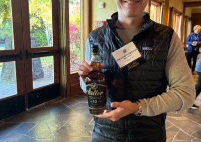 Oregon Geriatrics Society 2023 Conference - an attendee poses with a bottle of Weller bourbon - double doors with glass panes and window in background to left - rustic lodge