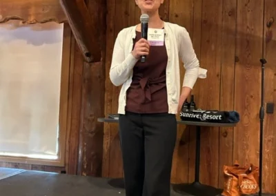 Oregon Geriatrics Society 2024 Conference - an attendee speaks into a microphone onstage in a rustic lodge with a projector screen in the background to the left