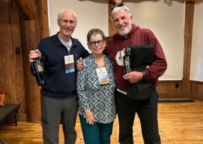 Oregon Geriatrics Society 2024 Conference - three attendees cheerfully pose with bottles of wine and a black Sunriver Resort folded hoodie - rustic lodge