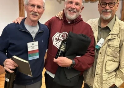 Oregon Geriatrics Society 2024 Conference - three attendees pose for a photo op while holding bottles of wine and a black folded Sunriver Resort hoodie - rustic lodge