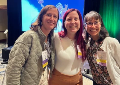 Oregon Geriatrics Society 2025 Conference - three attendees smiling and posing for a photo in front of a screen showing a still from the movie "Up" with an emerald green curtain in the background