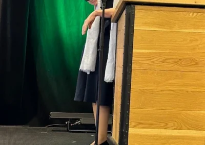 Oregon Geriatrics Society 2025 Conference - a woman leaning against a podium wearing red glasses and a white scarf speaking adjacently into a microphone