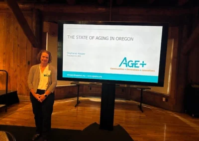 Oregon Geriatrics Society 2025 Conference - Stephanie Hooper standing to the left of a screen displaying the title card of her presentation, "The State of Aging in Oregon" -rustic lodge