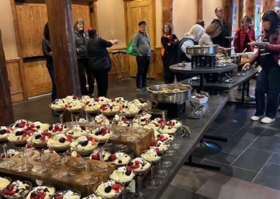 Oregon Geriatrics Society 2025 Conference - an arrangement of dessert parfaits in martini glasses in foreground, attendees lining up for buffet in background, rustic lodge