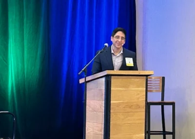 Oregon Geriatrics Society 2025 Conference - a man speaking at a podium in front of an emerald green curtain with a blue spotlight coming down from above.