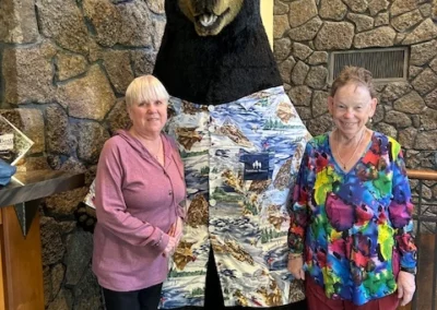 Oregon Geriatrics Society 2025 Conference - two attendees and a black bear costumed mascot pose near a stone wall inside a rustic lodge